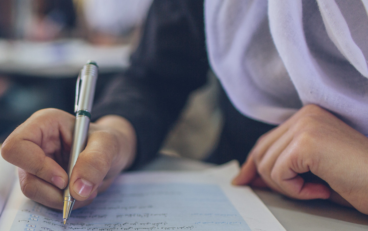 Young girl's hands writing in a notebook with a pen.